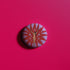 Circular pin featuring a nude goddess figure in gold against a red sunburst pattern on lavender background, with moon and star details